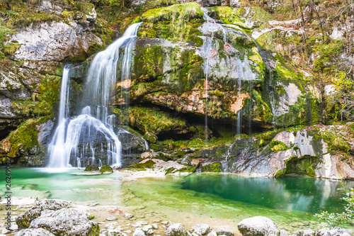 Beautiful natural clear flowing water waterfall covered with green moss colored in autumn season Virje, Slovenia