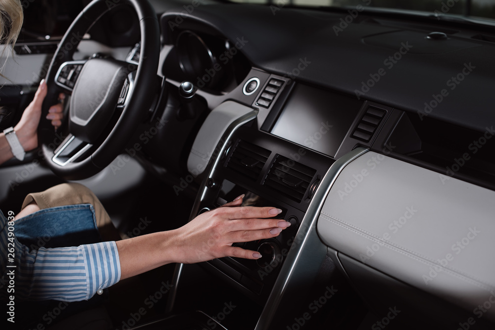 cropped view of young woman touching buttons while holding steering wheel in car cropped view of young woman touching buttons while holding steering wheel in car