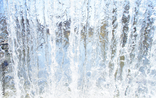 Transparent blue white water pours from above. View through the water wall of the waterfall for the background.