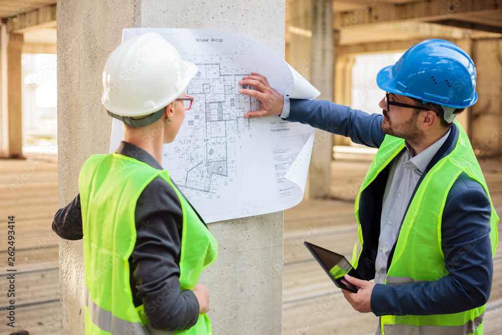 Team of successful young architects and business partners during a meeting on a construction site. Looking at architectural drawings and blueprints.
