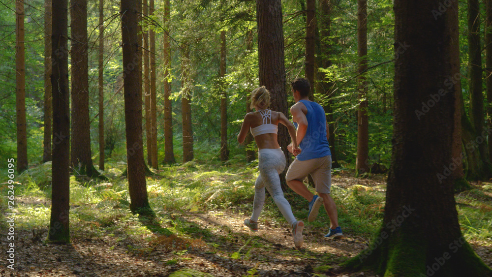 Fototapeta premium Unrecognizable woman in white sportswear and boyfriend jog through the forest.