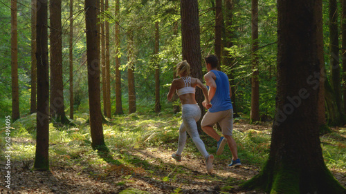 Unrecognizable woman in white sportswear and boyfriend jog through the forest.