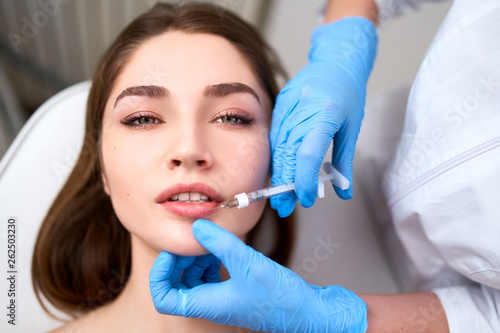 Lip Augmentation. Closeup Of Beautician Doctor Hands Doing Beauty Procedure To Female Lips with Syringe. Young Woman's Mouth Receiving Hyaluronic Acid Injection. Cosmetology Treatment. Filler Therapy.