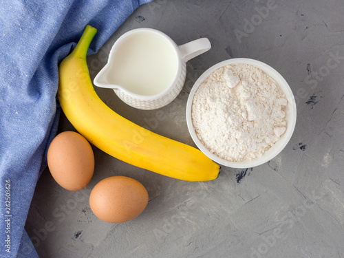 The ingredients for the banana cake on gray background. Wooden Spoon, Banana, Eggs, Milk