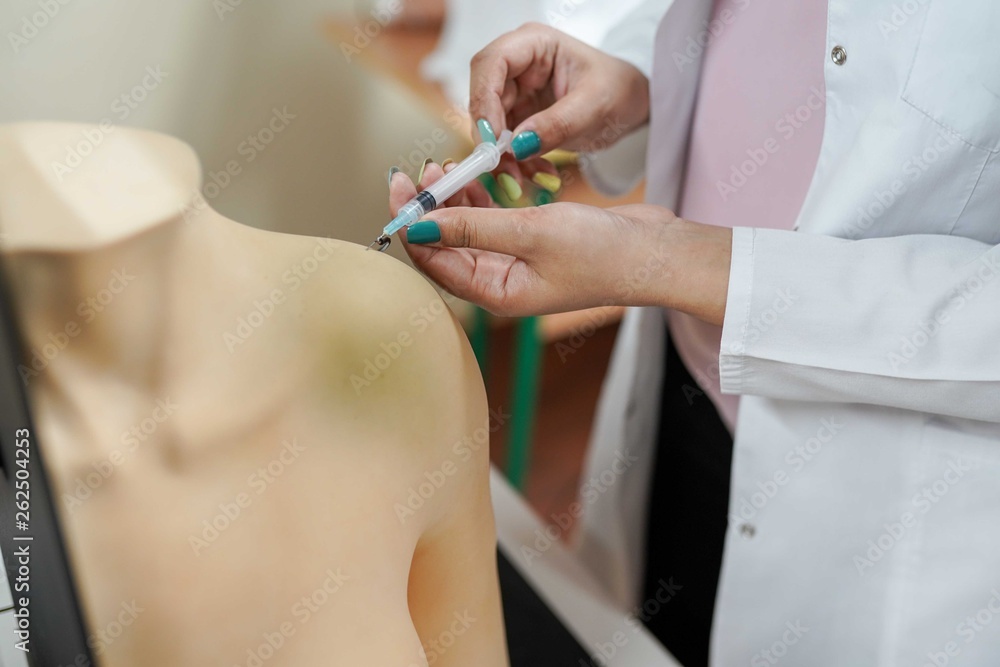medical background.Nursing student practicing blood taking on mannequin hand under instructor supervision medical background.Nursing student practicing blood taking on mannequin hand under instructor supervision