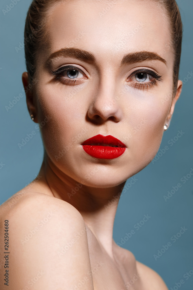 Close-up portrait of beautiful young female face with perfect and clean skin, underlined eyes and red lips against blue studio background. Concept of beauty, care, treatment, health, spa, cosmetics. Close-up portrait of beautiful young female face with perfect and clean skin, underlined eyes and red lips against blue studio background. Concept of beauty, care, treatment, health, spa, cosmetics.