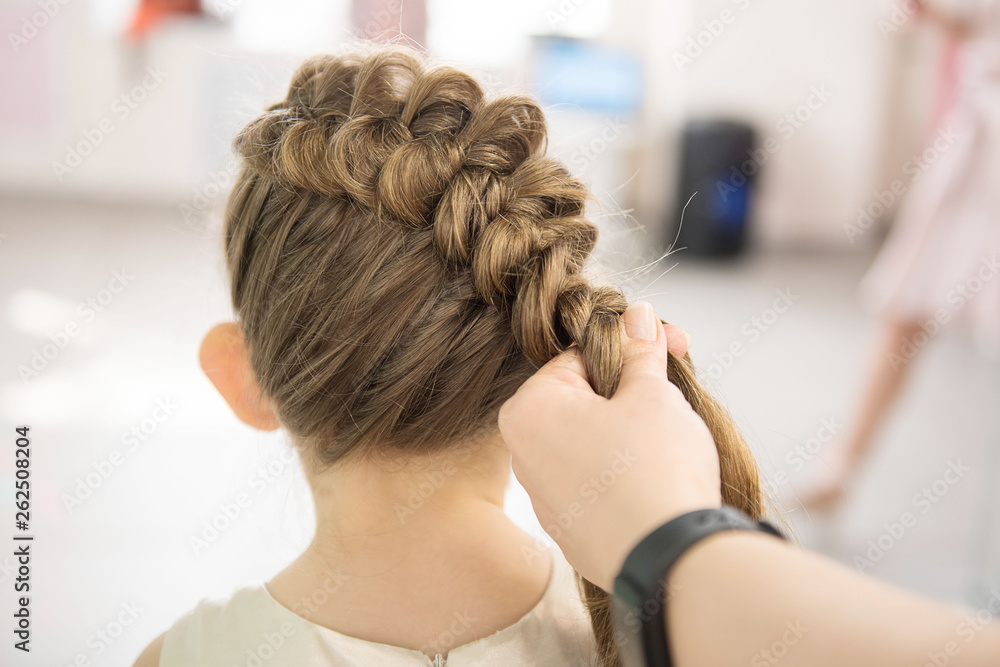 Fototapeta premium Hairdresser weaving plaits in beauty salon. Hairdressing services. Сreating hairstyle. Hair styling process. Children's hairdressing salon.