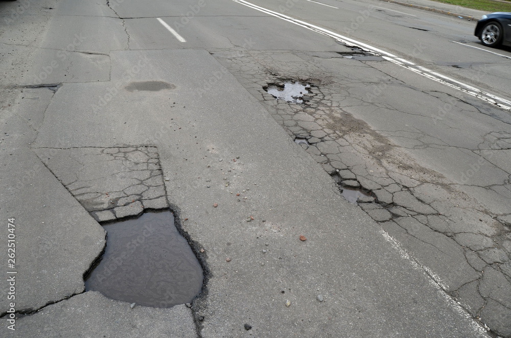 Fototapeta premium Poor condition of the road surface. Spring season. Hole in the asphalt, risk of movement by car, bad asphalt, dangerous road, potholes in asphalt. Kiev,Ukraine