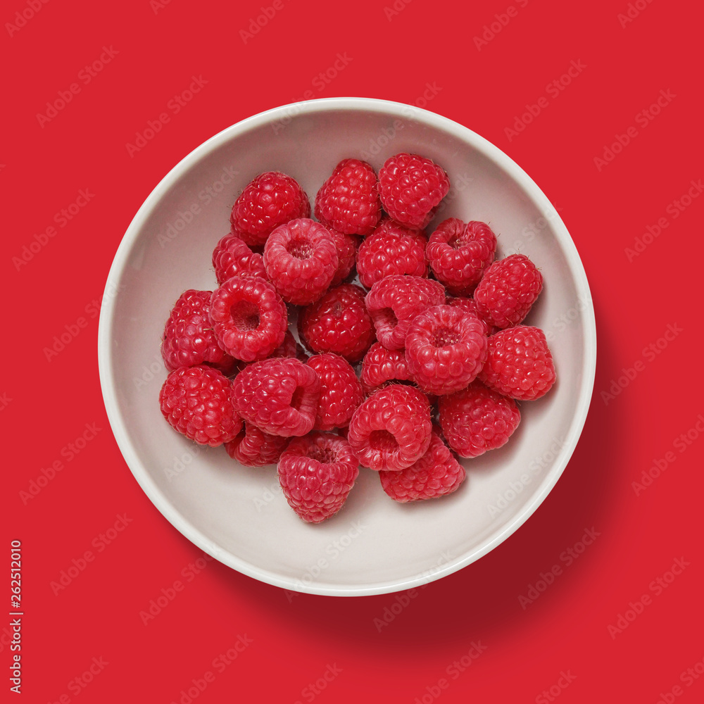 Closeup of raspberry in a white porcelain bowl isolated on red background Closeup of raspberry in a white porcelain bowl isolated on red background