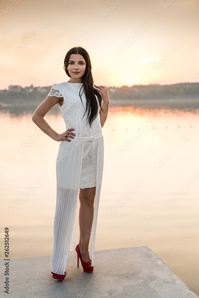 Young beautiful woman in dress posing at sea coast at sunset Young beautiful woman in dress posing at sea coast at sunset