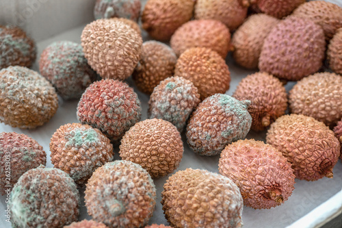 Rotten lychee fruit in a wooden drawer on a rustic wooden background. Fruits are covered with mold. Close-up