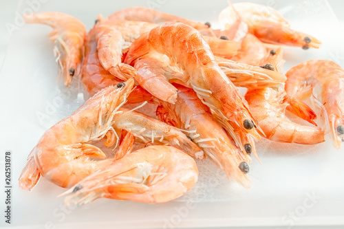 Shrimps lie on a small glass transparent plate on a bright table