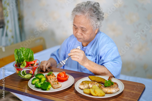 Asian senior or elderly old lady woman patient eating breakfast healthy food with hope and happy while sitting and hungry on bed in hospital.