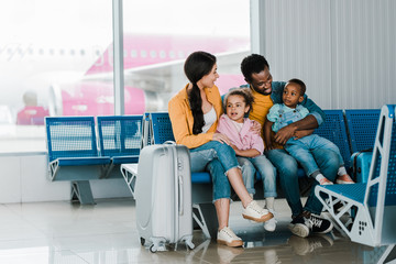 smiling african american family with baggage and kids sitting in airport