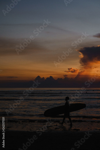 Surfer silhouette walking across the sea shore at sunset