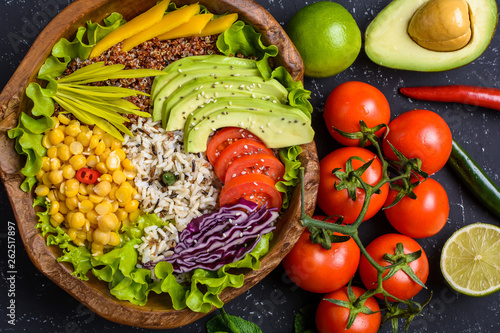 Healthy vegan superfood bowl with quinoa  wild rice  chickpea  tomatoes  avocado  greens  cabbage  lettuce on black stone background top view. Food and health