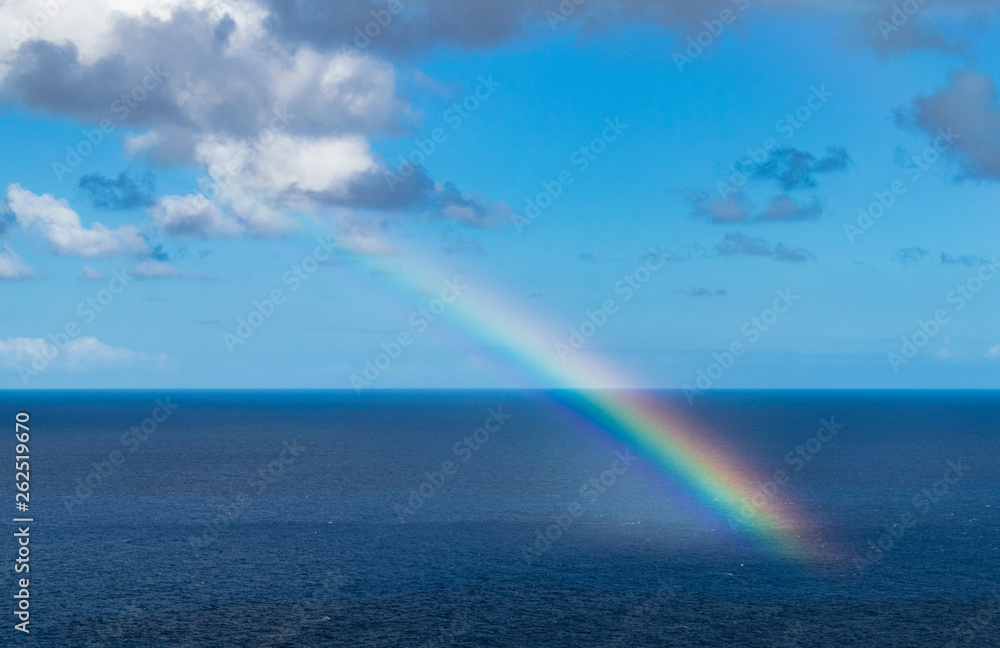 Rainbow in the Atlantic ocean, with blue sky and with clouds