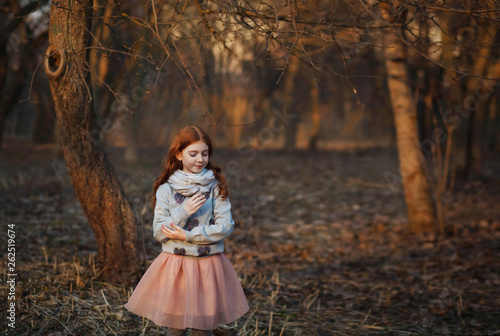 Portrait of a cute red-haired girl with freckles standing in an autumn or spring park or forest. Inspiration and dreams