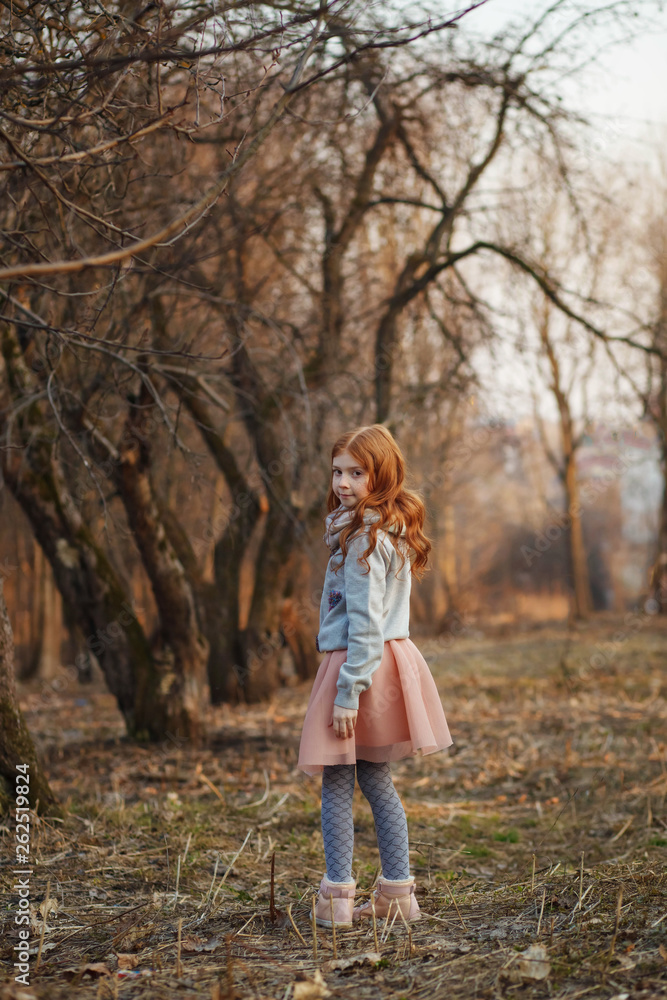 Red-haired girl with freckles in a park. Spring or Autumn. Happy carefree childhood.