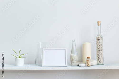 Shelf against white wall with decorative candle, glass and rocks. Potted spider plant. © MexChriss