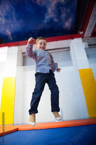 happy smiling small caucasian boy jumping on indoors trampoline during leisure sport training workout