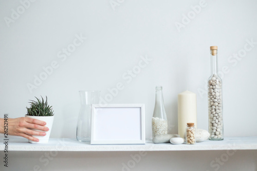Shelf against white wall with decorative candle, glass and rocks. Hand putting down potted succulent plant. © MexChriss