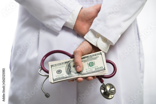 Medical doctor holding money and stethoscope in hospital setting