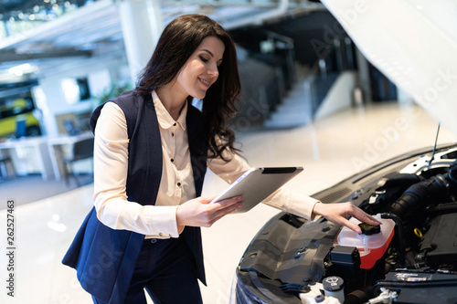 Beautiful sale-manger inspect new car with help of tablet in dealership center