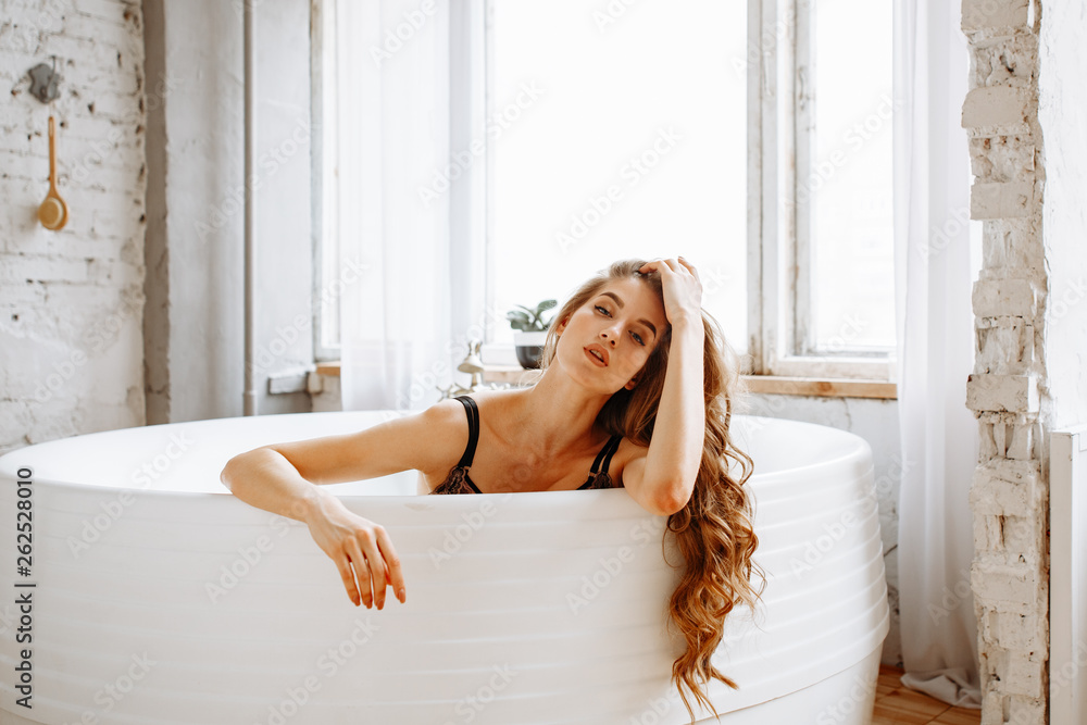 Naklejka premium Beautiful girl with long curly hair in sexy underwear posing on bathroom background. 