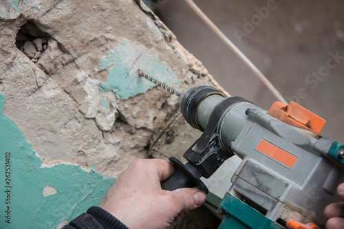 Repair and construction working indoors. Grunge background rubble and stones. Man's hands with a drill make a hole in the concrete. Surface preparation for work.