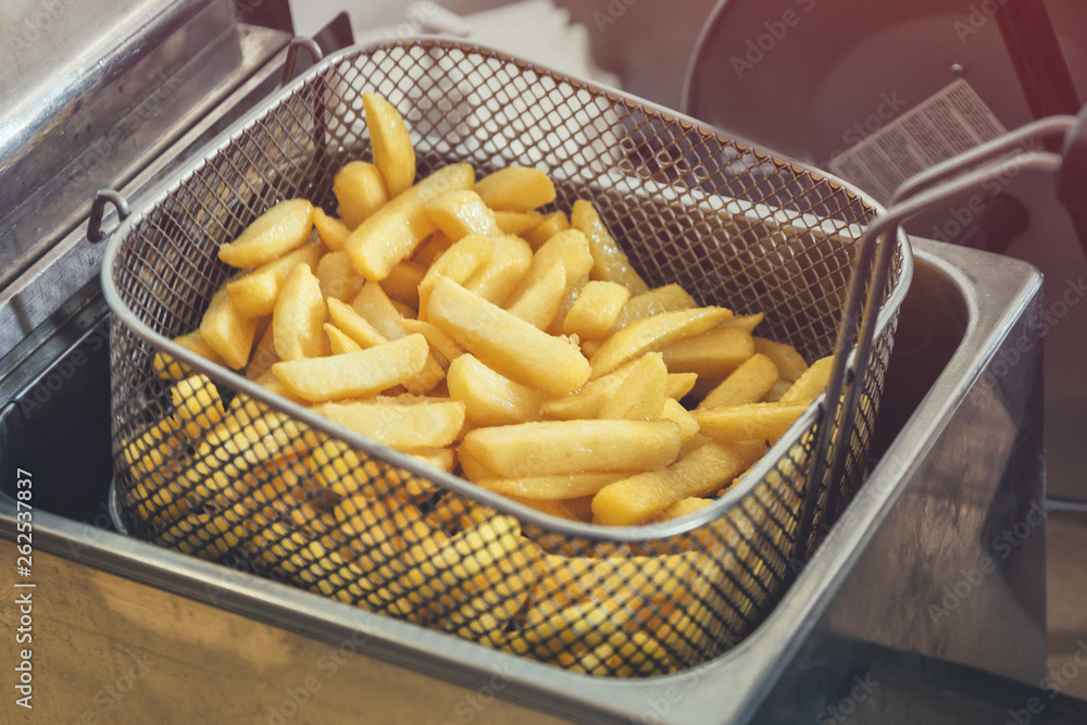 French fries cooking. Grid with strips of potato lowered into boiling oil. The concept of fast food. Belgian frit