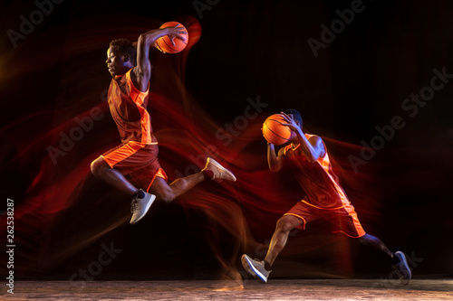 Two steps for winning. African-american young basketball player of red team in action and neon lights over dark studio background. Concept of sport, movement, energy and dynamic, healthy lifestyle.