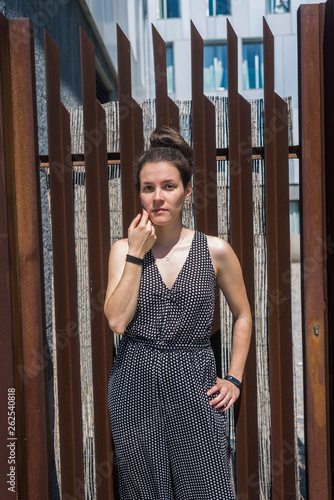 Pretty young stylish woman standing against a fence