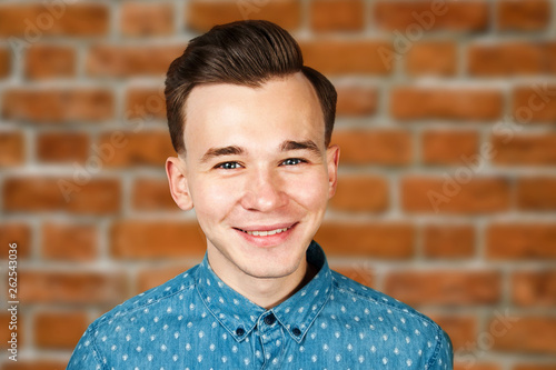 smiling portrait white young guy model dressed in blue shirt looking at the camera on brick wall background