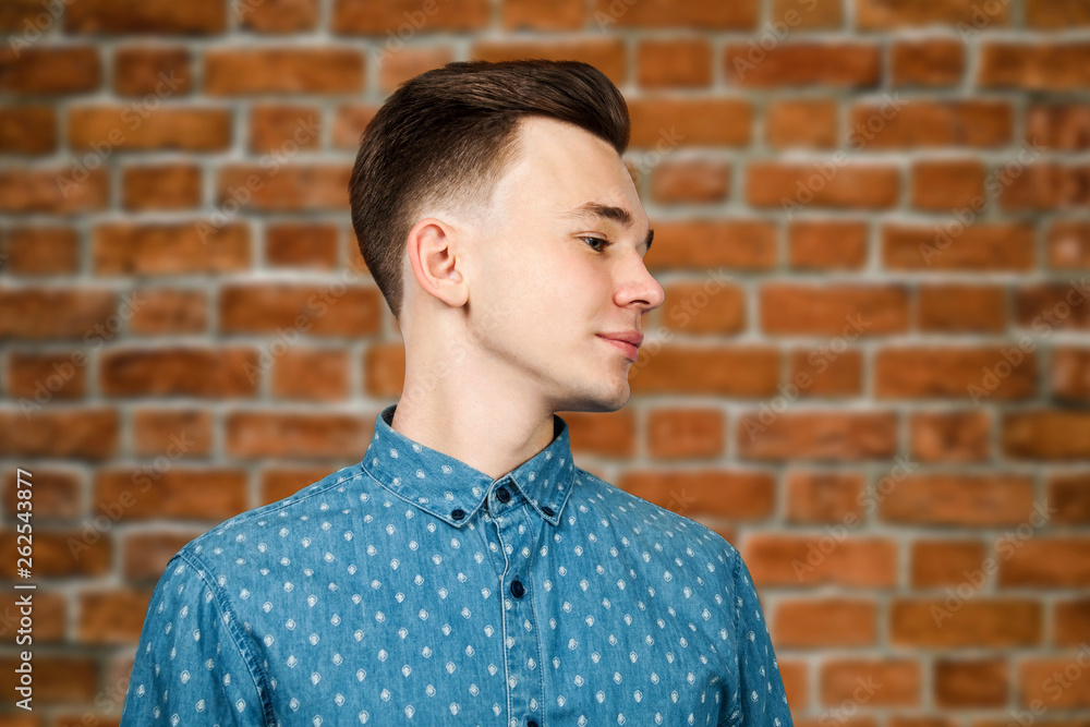 White young guy dressed in blue shirt on brick wall background smiles and looking aside White young guy dressed in blue shirt on brick wall background smiles and looking aside