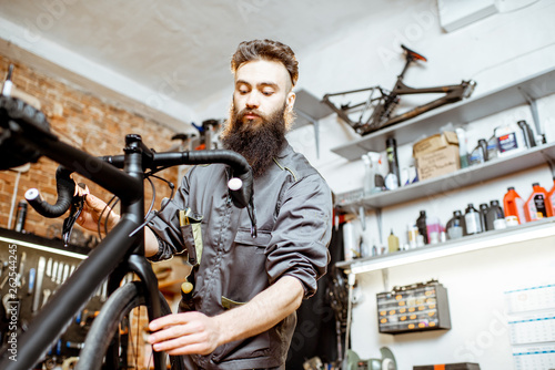 Handsome bearded repairman in workwear serving a sports bike at the bicycle workshop