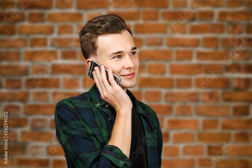 White young guy writes a message on the mobile phone and smiles. Man on brick wall background