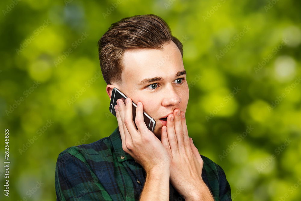 portrait of scared White young guy writes a message on the mobile phone and smiles. Man on green bokeh background portrait of scared White young guy writes a message on the mobile phone and smiles. Man on green bokeh background