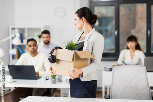 business, firing and job loss concept - sad fired female employee with box of personal stuff leaving office looking at her colleagues © Syda Productions