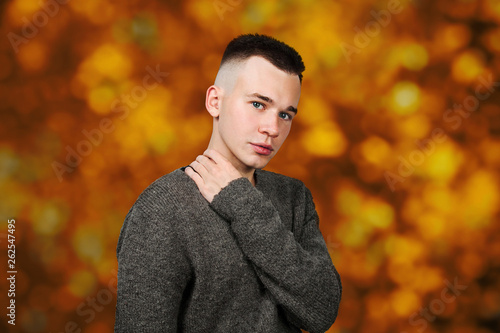 Portrait of white yong guy in gray sweater and short haircut, on orange, red autumn background