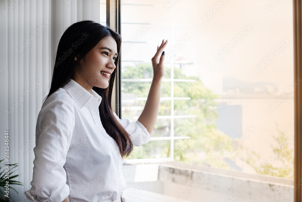 The beauty woman put her hand touch the mirror,looking outside with smile and happy face,having a rest between work at office,relax time The beauty woman put her hand touch the mirror,looking outside with smile and happy face,having a rest between work at office,relax time