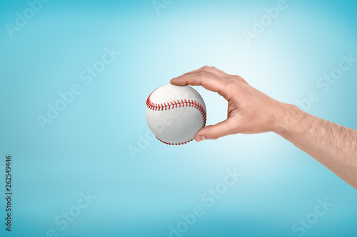 Side view of man's hand holding white baseball on light-blue background with some copy space.