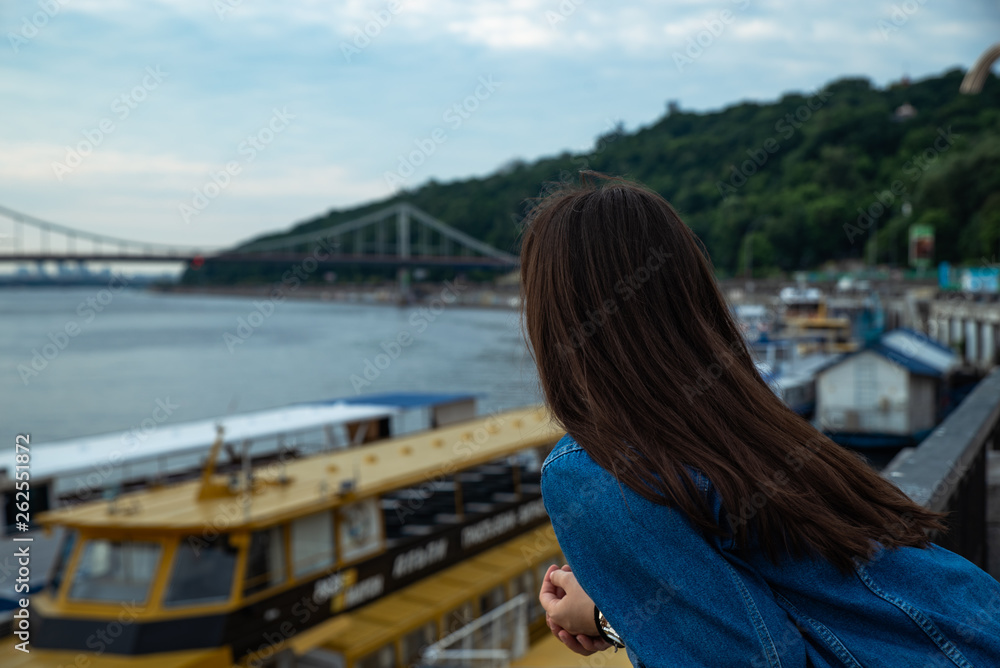 young pretty woman looking on river at morning time. boats in dock