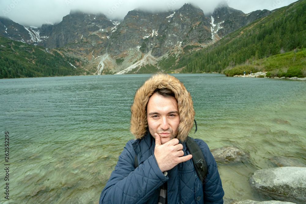 Suspicious young man  by the lake surrounded by mountains