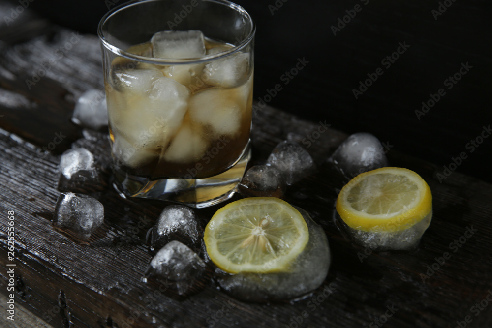 Whiskey with ice in a glass on a black wooden old background with ice and lemon Whiskey with ice in a glass on a black wooden old background with ice and lemon