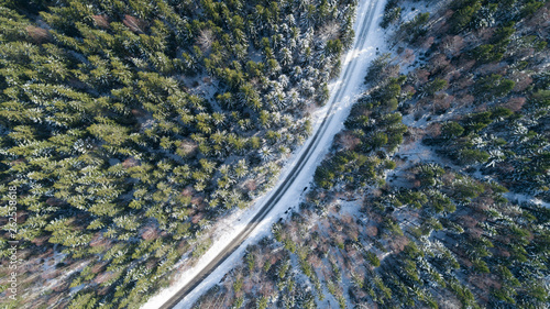 Aerial view of road through snow fir forest in winter. Shot. Aerial view deep winter rural country landscape flying over along deserted road through dense forest trees covered with fresh snow. 