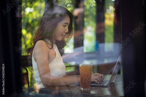 Young Asian woman working with laptop on the table, business concept, shot through the glass window