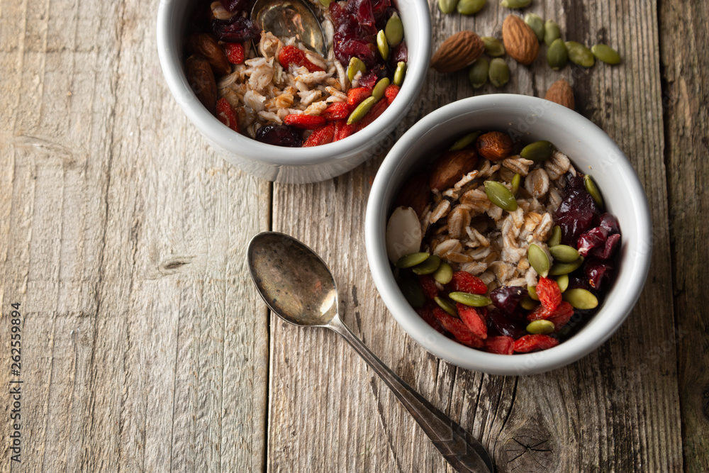 Healthy breakfast.Two bowls of muesli with oats, nuts and dried fruits - apples, resins, pumpkin seeds and almonds on wooden table. Top view. Rustic style. Healthy breakfast.Two bowls of muesli with oats, nuts and dried fruits - apples, resins, pumpkin seeds and almonds on wooden table. Top view. Rustic style.