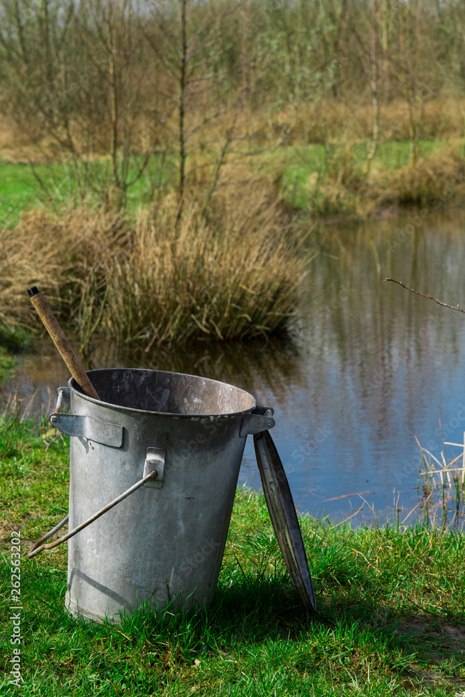 metal trash bin, bucket on green grass field, with ditch metal trash bin, bucket on green grass field, with ditch