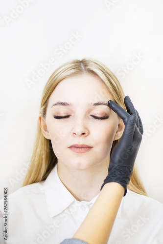 Female cosmetologist performs eyebrow correction on beautiful models in the beauty parlor. The girl's face is a blonde. Close-up. Facial care